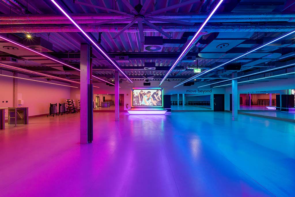 Großer, offener Kursraum im FitX Fitnessstudio Mülheim-Stadtmitte. An der hinteren Wand befindet sich eine erhöhte Bühne, dahinter eine Leinwand. Links und rechts davon sind Spiegelwände.