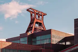 Blick auf die Zeche Zollverein in Essen bei Tag mit dem markanten roten Förderturm im Hintergrund.