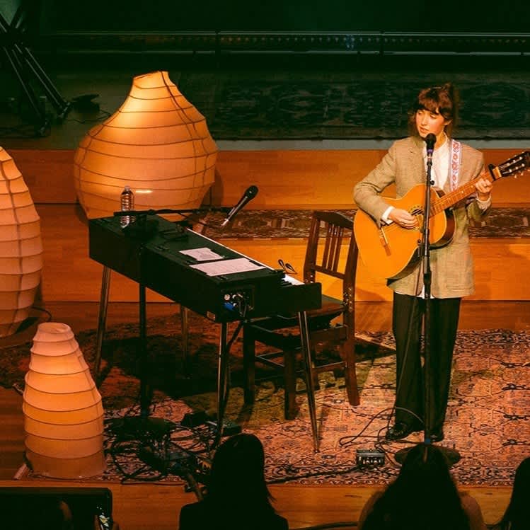 Clairo performing on stage, surrounded by custom Noguchi-inspired lamps.