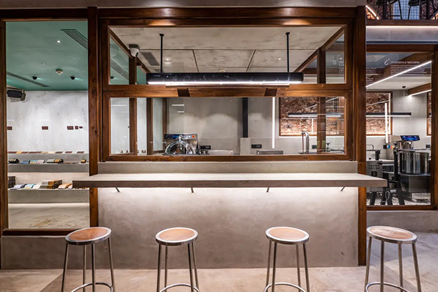 Renderizado de V-Ray que muestra una zona de cafetería con banquetas de bar bajo focos con una zona de cocina al fondo.