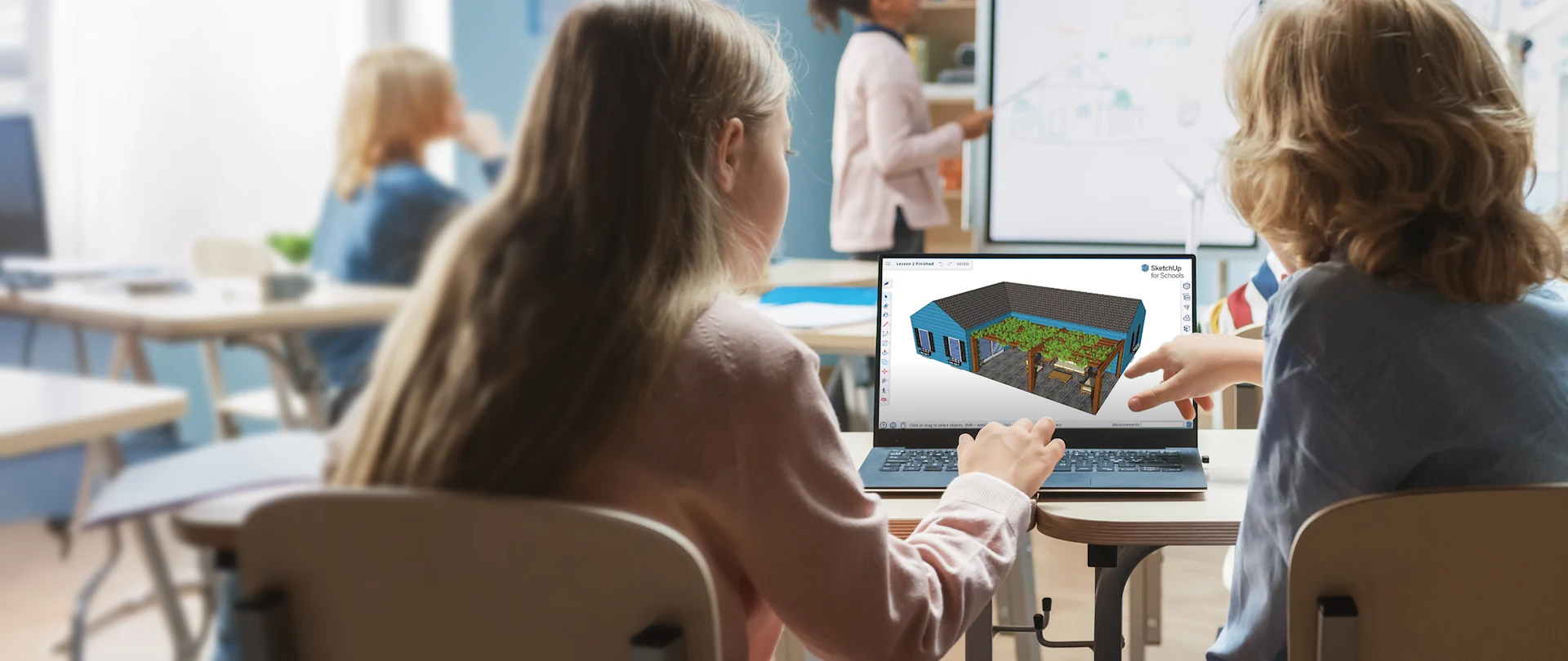 A student and teacher look at a laptop displaying a 3D model in SketchUp for Schools in a classroom.