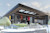 SketchUp model of the exterior of a modern wooden and glass building, showing steps, greenery, and people walking in the area.
