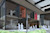 Close-up on a SketchUp render showing the entrance and patio of a commercial building with many windows, 2D scale figures, and some greenery.