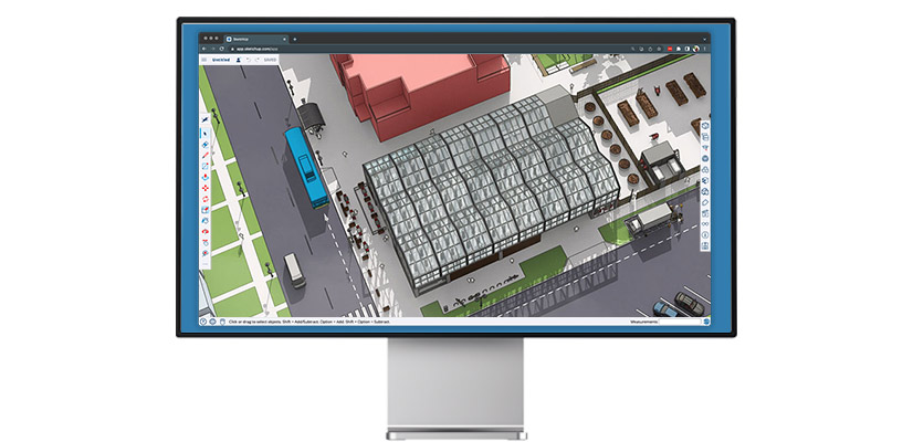 Monitor exibindo o SketchUp para web com um modelo arquitetônico 3D de um edifício moderno em um cenário urbano com ônibus, carros e prédios.