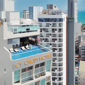 Una vista aérea del edificio blanco de Le's Cham Hotel en una ciudad densa, con una piscina infinita en la azotea que cuenta con reposeras y vistas al océano.