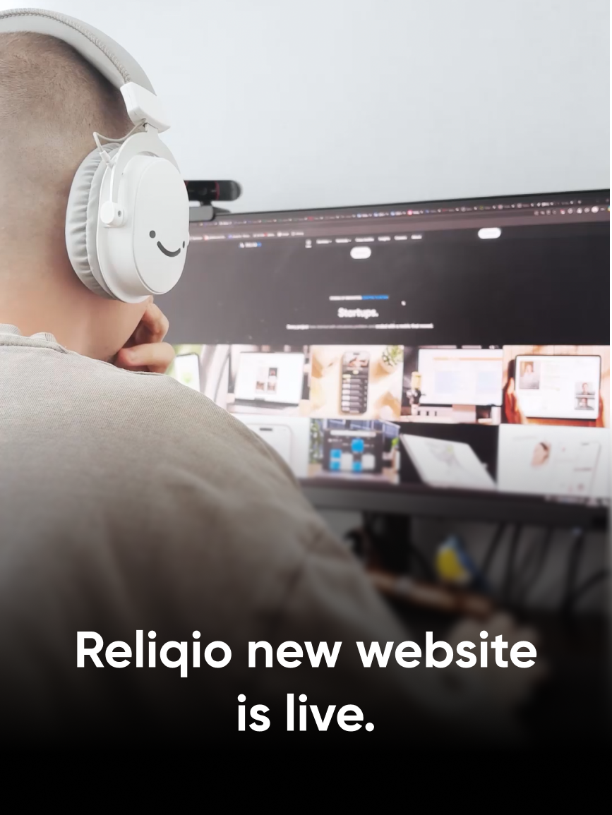 A designer at Reliqio in white headphones browsing the new Reliqio website on a desktop monitor, with the title "Reliqio new website is live."