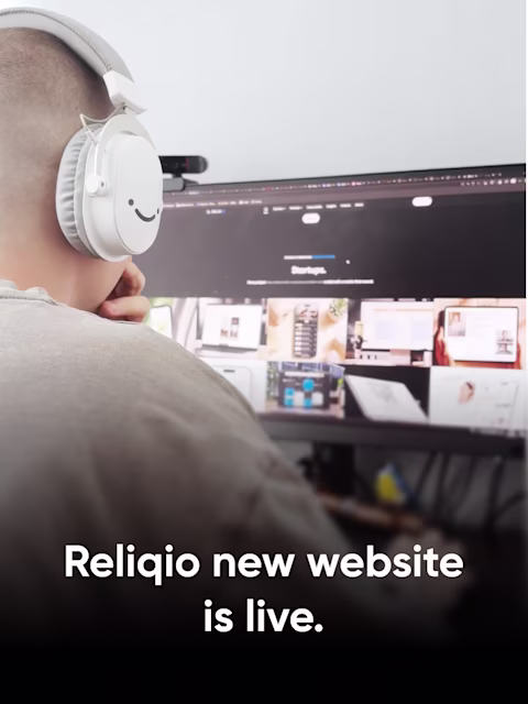 A designer at Reliqio in white headphones browsing the new Reliqio website on a desktop monitor, with the title "Reliqio new website is live."
