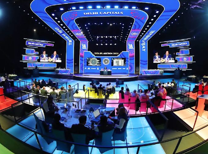 The IPL auction floor — a wide hall with team tables, screens displaying player names and bids
