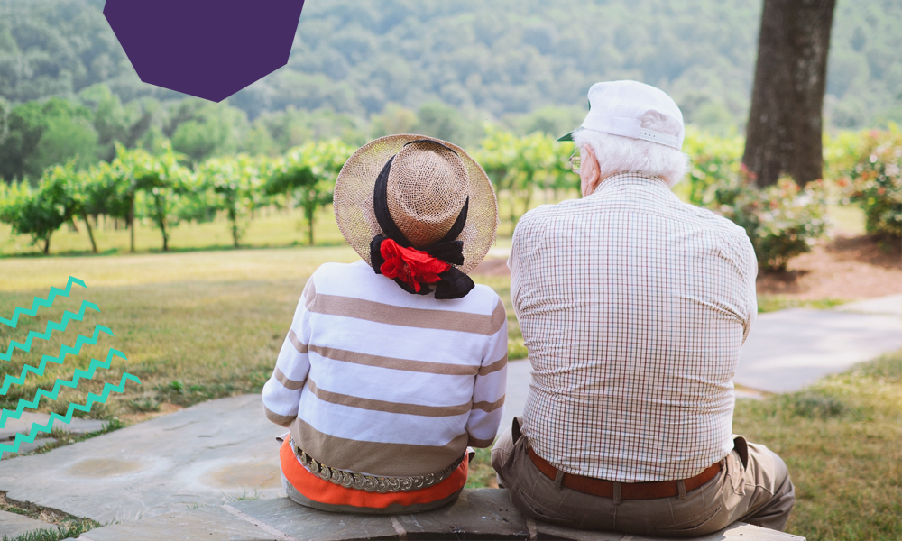 Older couple sitting on a big stone looking at mountains together