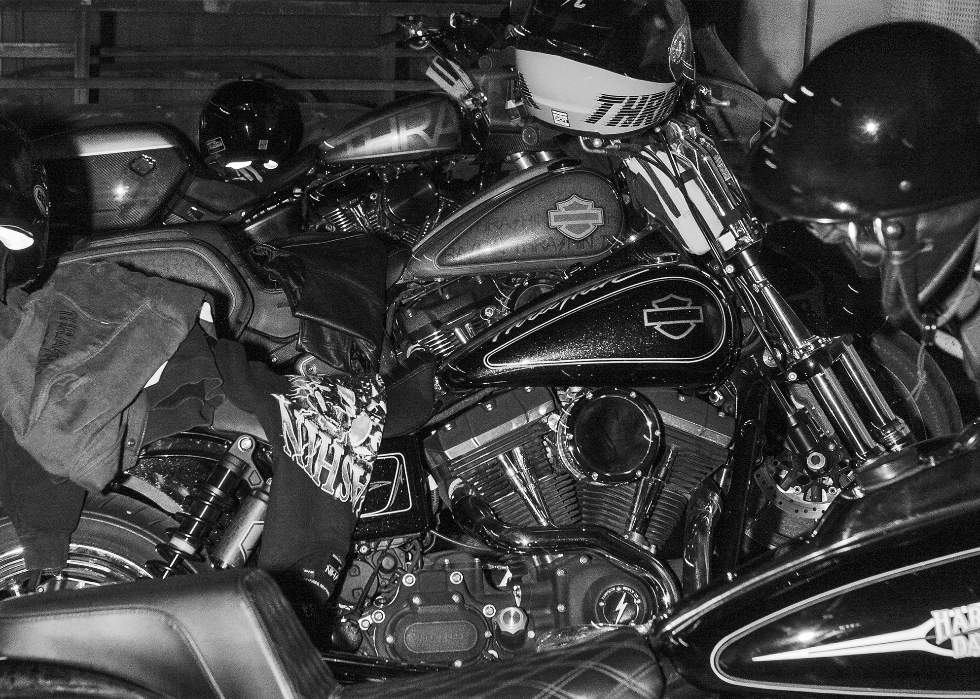A close up shot of 4 Harleys with clothes and helmets draped over them, in black and white.