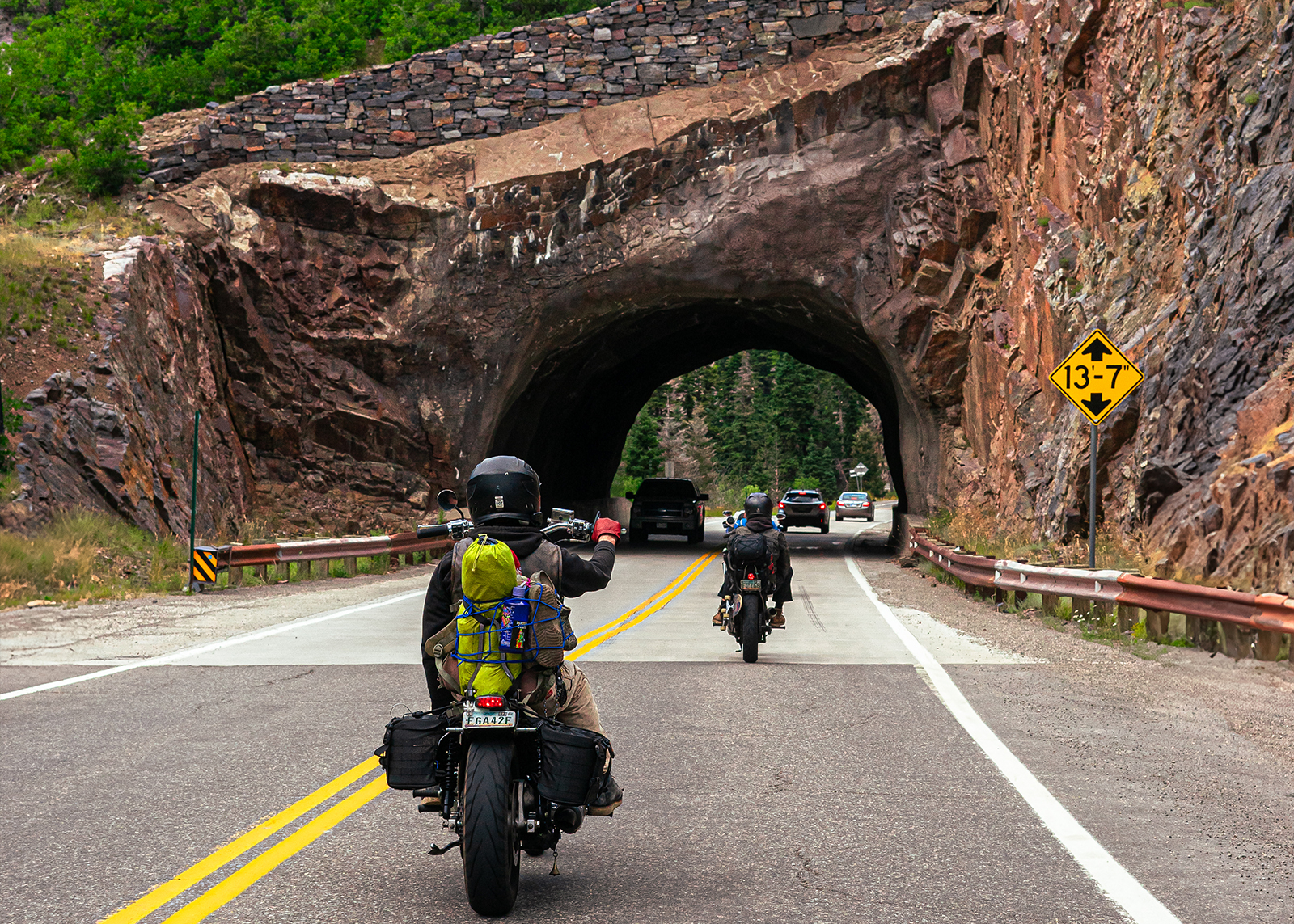 Two vintage choppers head toward a tunnel cut through a mountainside