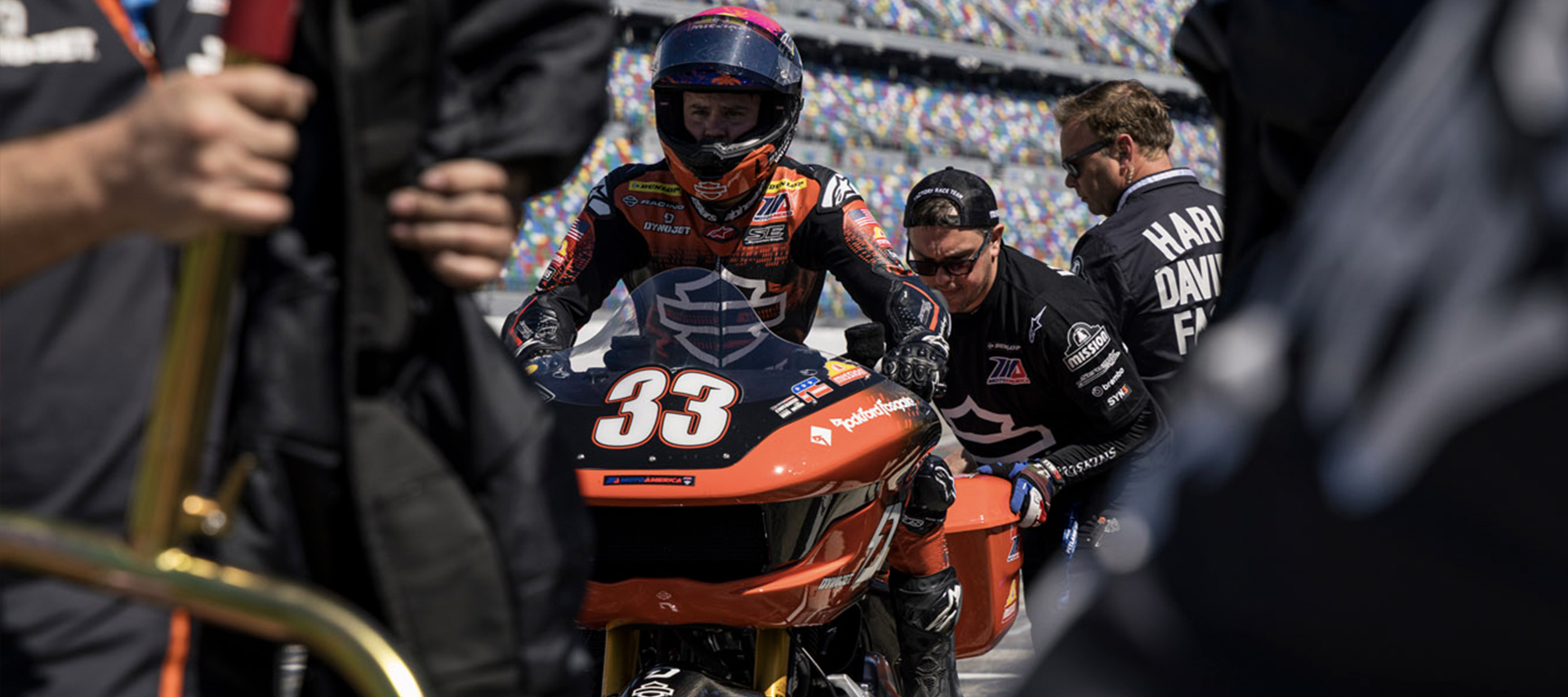 Kyle Wyman sits on his motorcycle in pit lane at Daytona Raceway, surrounded by his race crew.