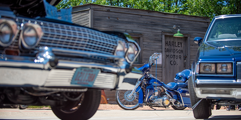Custom blue chopper motorcycle between classic cars outside Harley-Davidson Motor Co. building