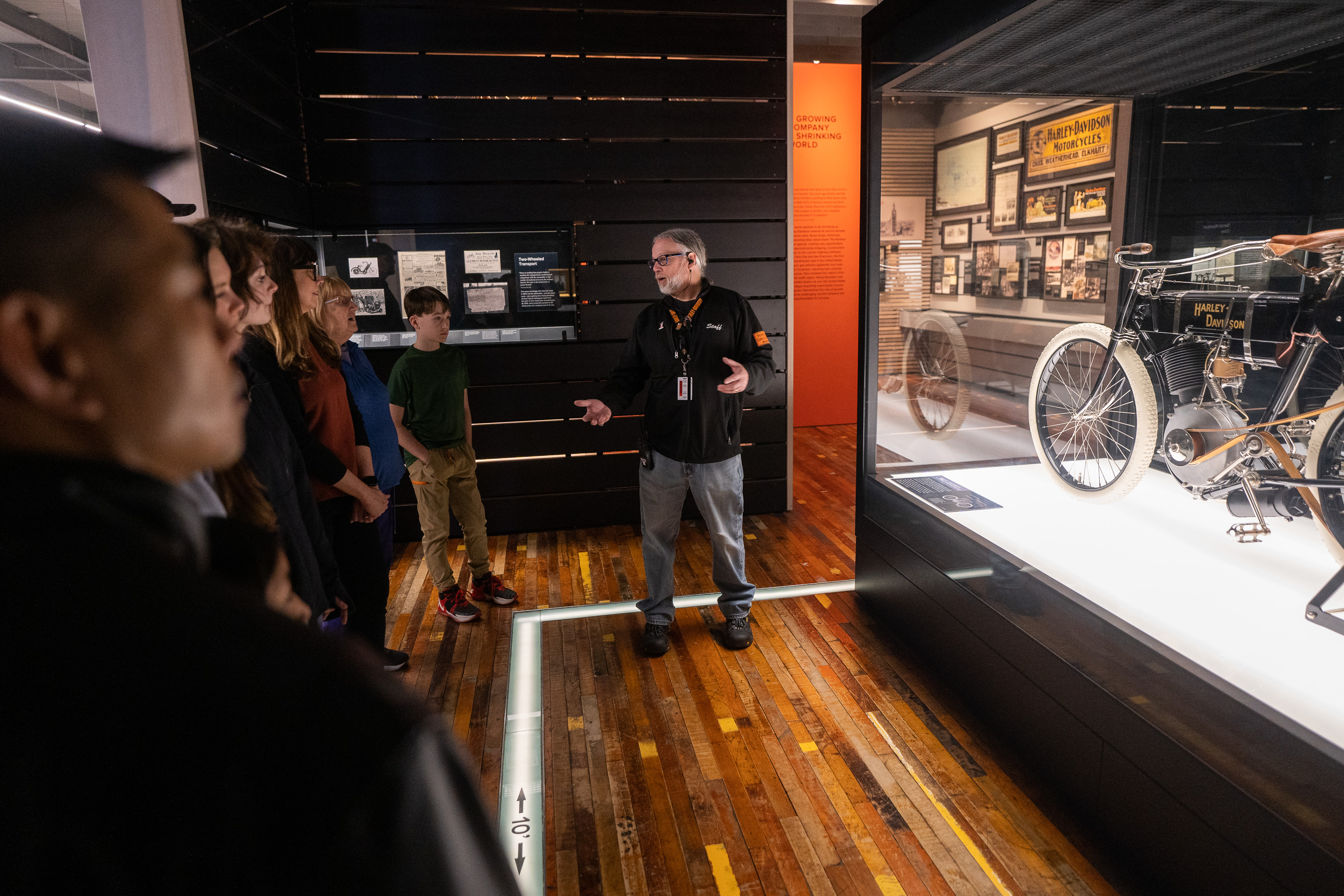 Guía del museo hablando con los visitantes junto a la exhibición de motocicletas Harley-Davidson vintage