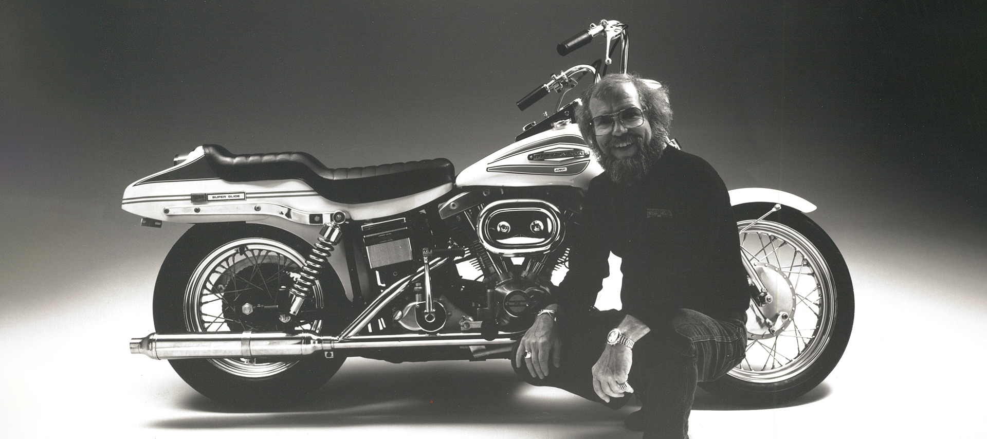 Willie G squats in front of a Super Glide 