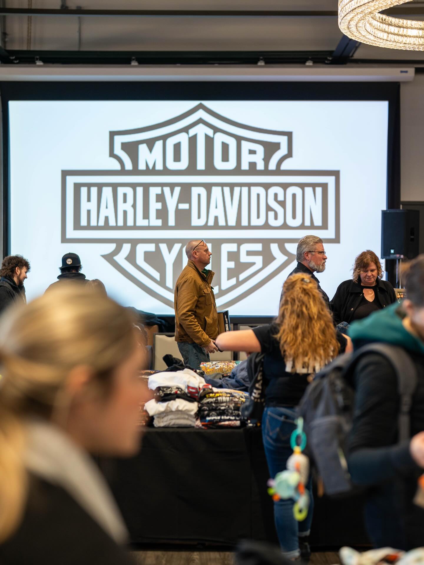 Visitantes comprando en una venta de outlet de fábrica frente a una exhibición con el logotipo de Harley-Davidson