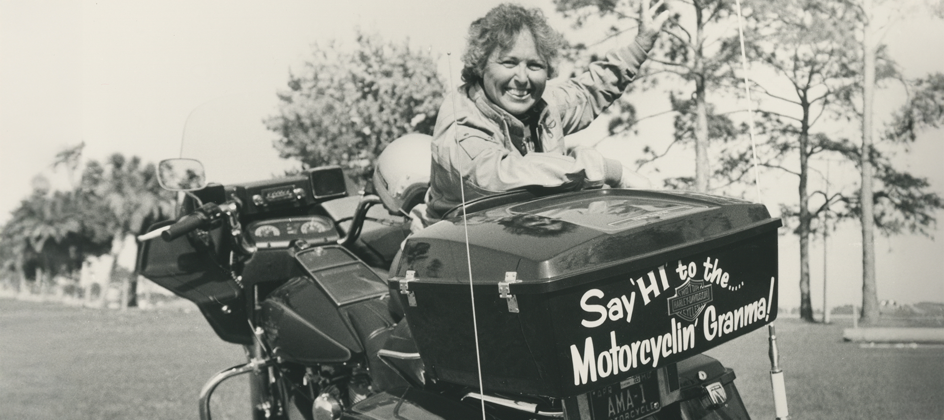 A vintage photo of Motor Maid Hazel Kolb and her motorcycle with a sticker on the back that says “Say hi to the... motorcycin’ granma!”