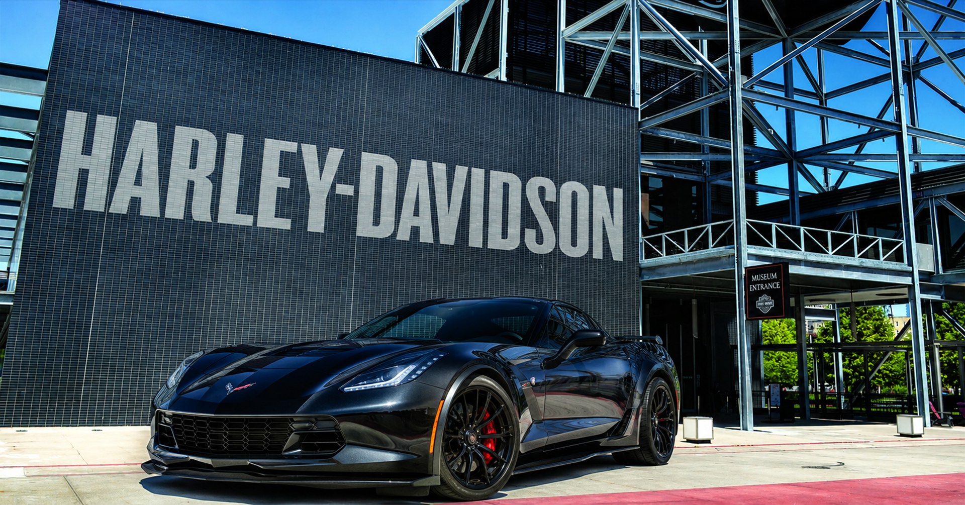 Black sports car parked under Harley-Davidson sign outside museum entrance