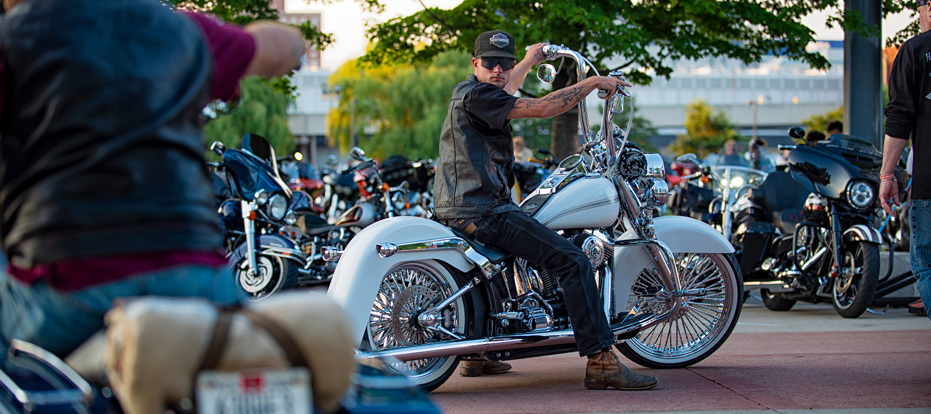 Pessoa em motocicleta Harley-Davidson personalizada com guidão elevado em encontro de motos ao ar livre