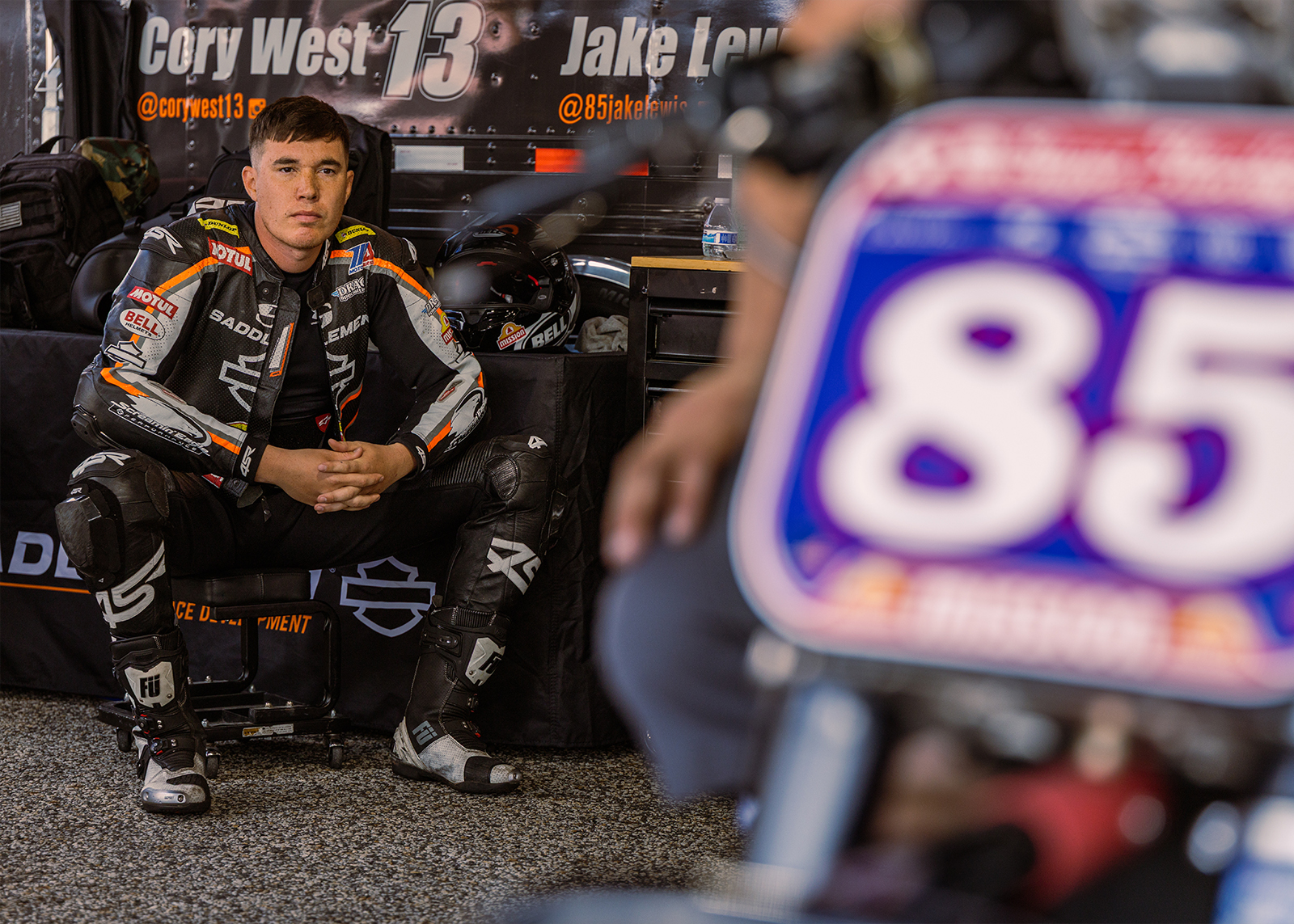 One of the racers sits in the garage and looks at his bike, which is just out of focus in the foreground.