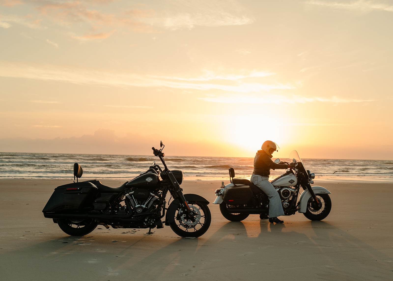 A woman sits on her motorcycle on the beach at sunrise
