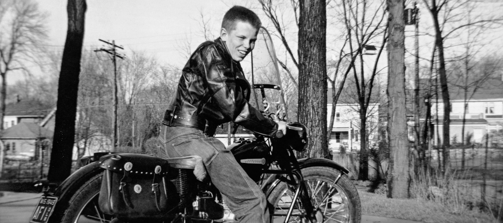 A teenaged boy in a leather jacket sits on a motorcycle