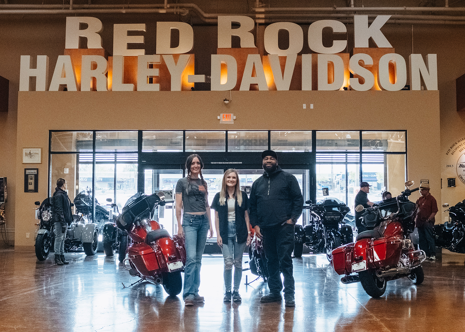Three staff members pose in front of a big Red Rock Harley-Davidson sign on the showroom floor.