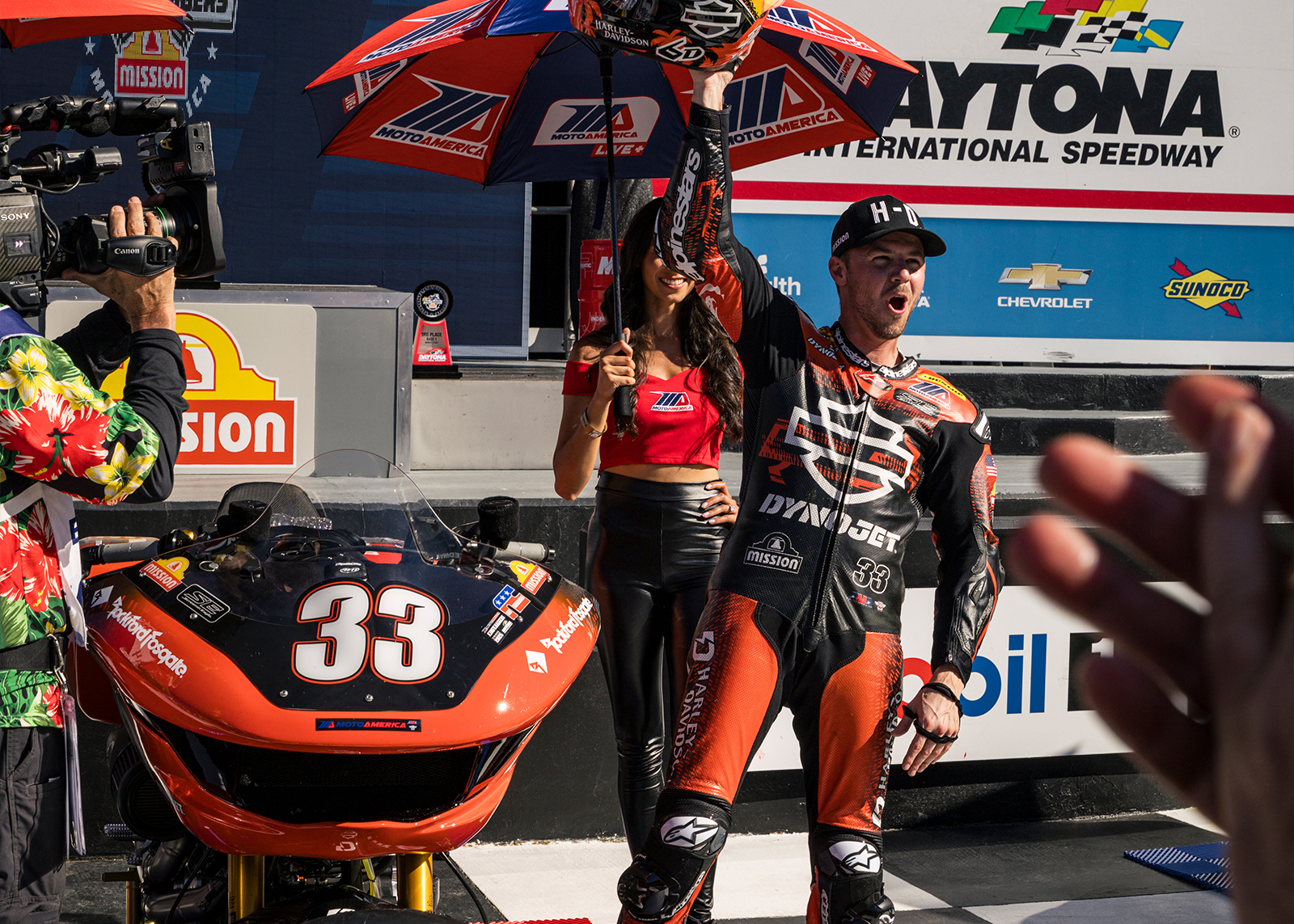 Kyle Wyman shouts in celebration with his helmet in the air in Victory Circle 