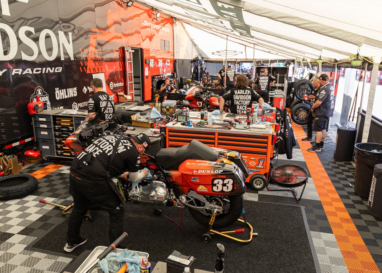 Inside the HD team’s garage, two bikes are being cleaned and worked on, while other members of the race team stand in conversation.