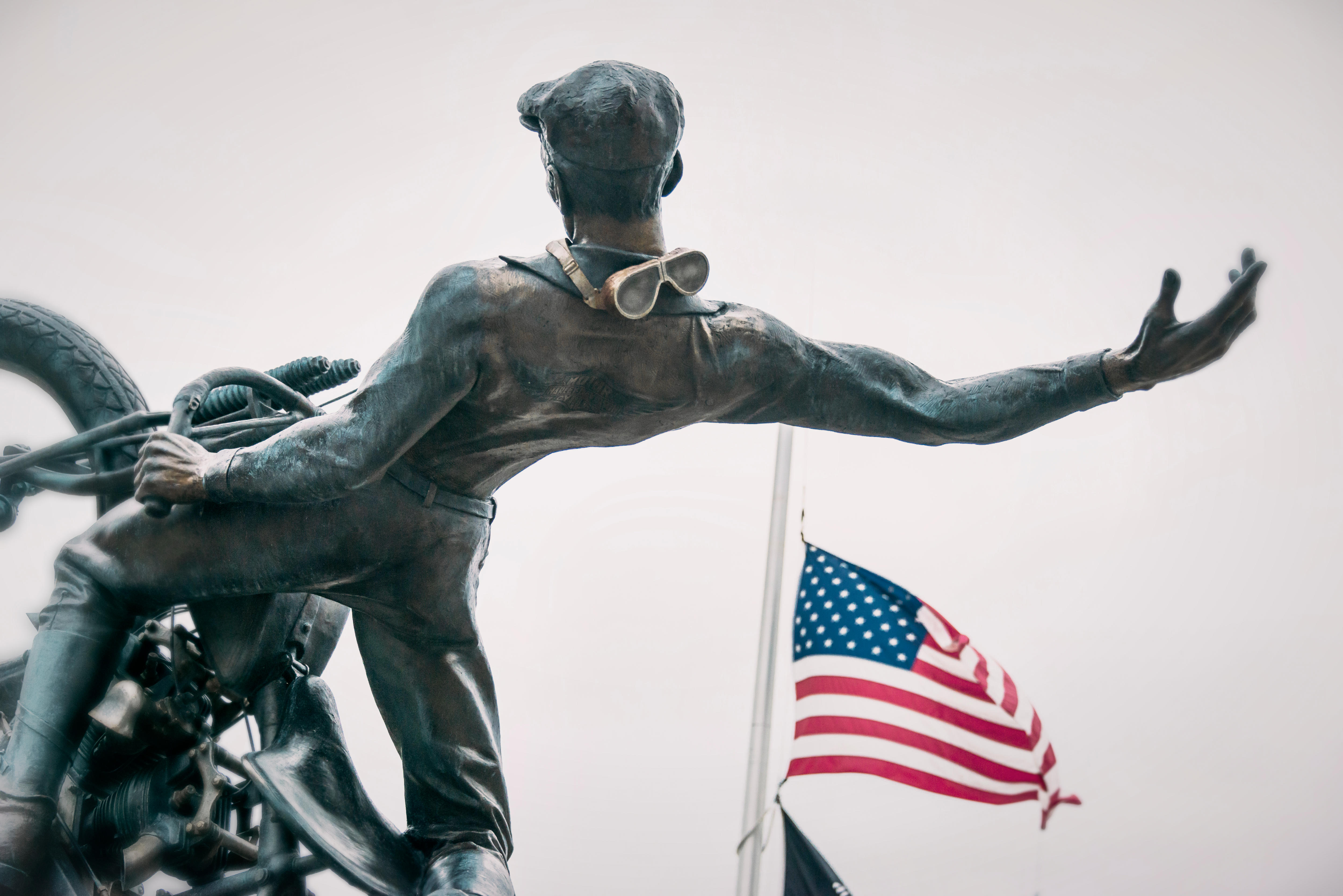 Estátua de motociclista com o braço estendido e bandeira americana ao fundo