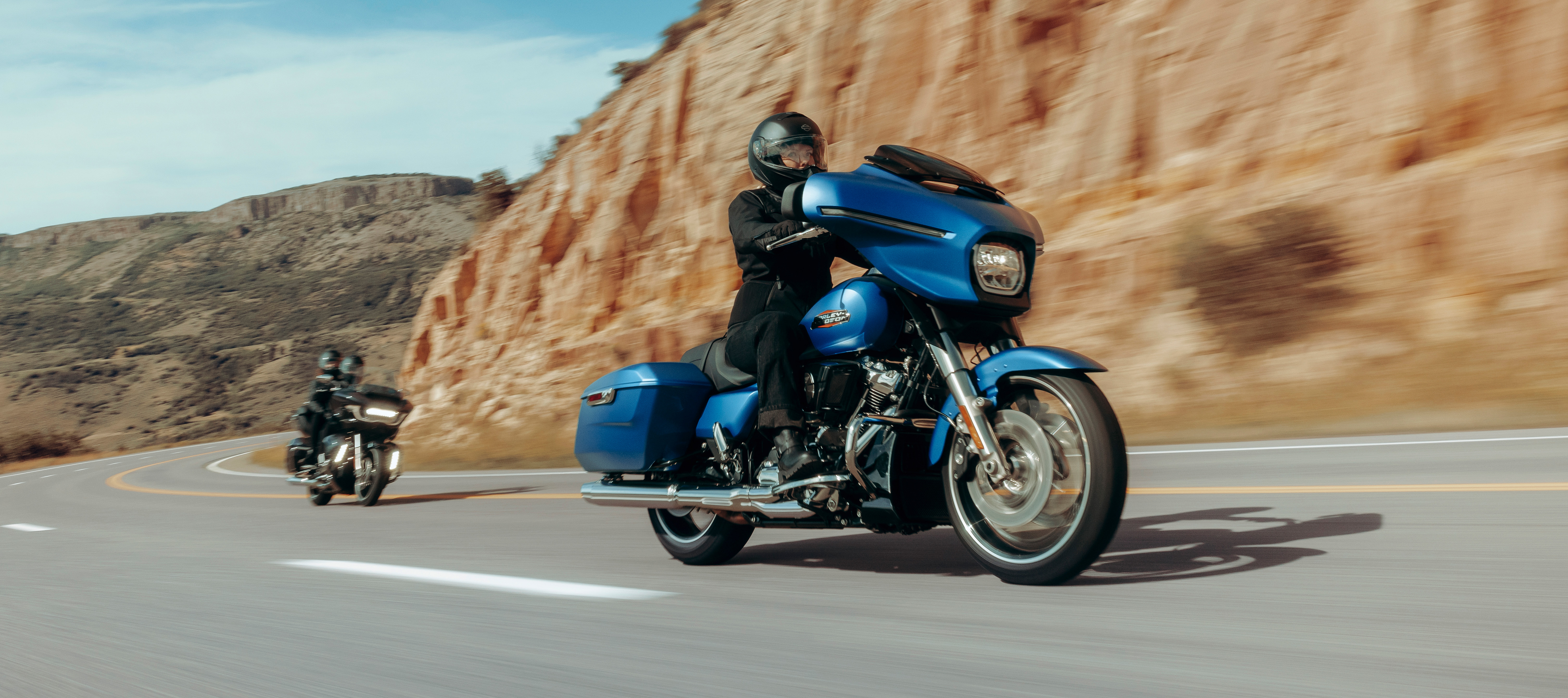 Motocycliste sur une motocyclette de tourisme Harley-Davidson bleue en tête sur une route désertique sinueuse