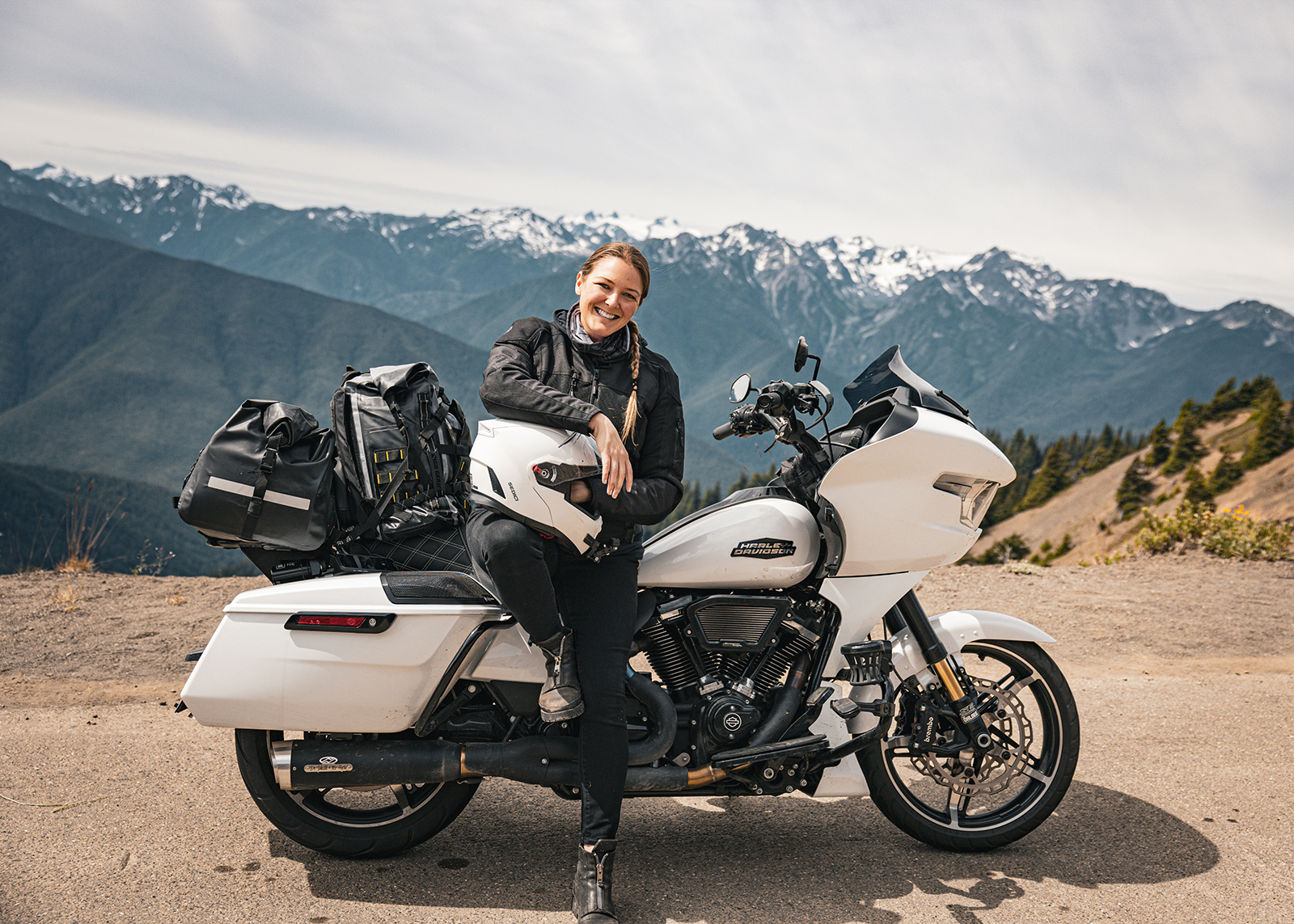 The author leans on her white Harley-Davidson Road Glide motorcycle with snowy mountains behind her.