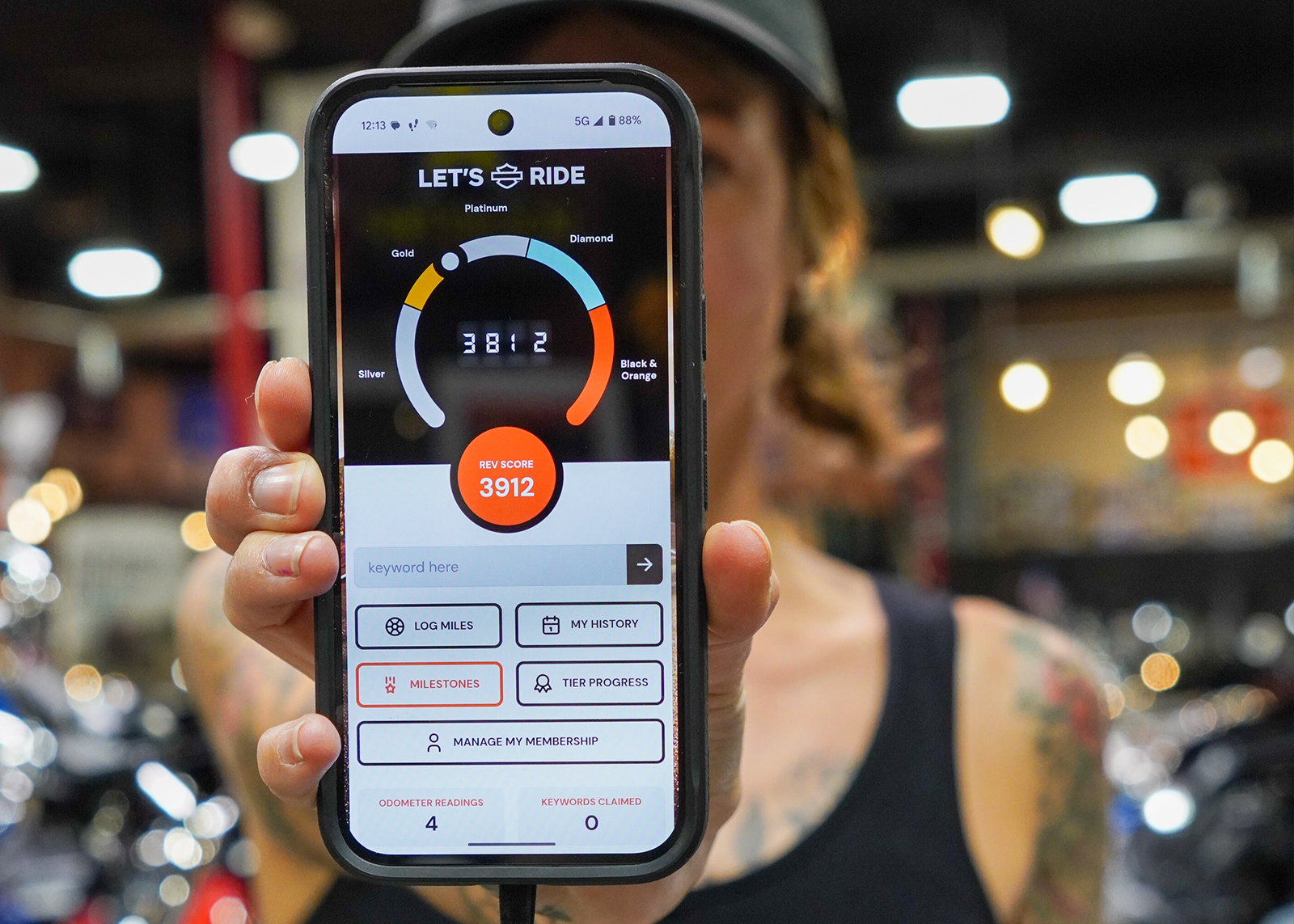 The author Sanna Boman holds her phone to the camera showing the statistics from her Harley-Davidson Let’s Ride app profile.