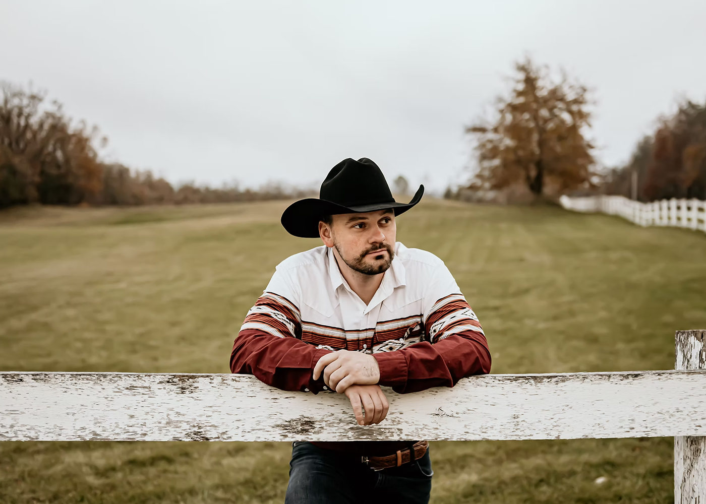 Person in cowboy hat leaning on fence in open field