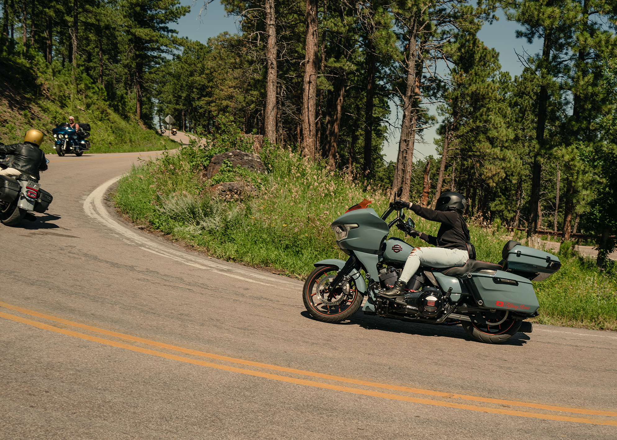 Motorcyclists navigate a sharp curve on a scenic forested mountain road.