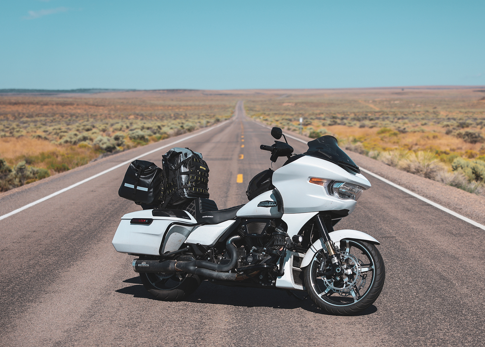 White Harley-Davidson Road Glide motorcycle with luggage parked on an empty desert highway under blue sky.
