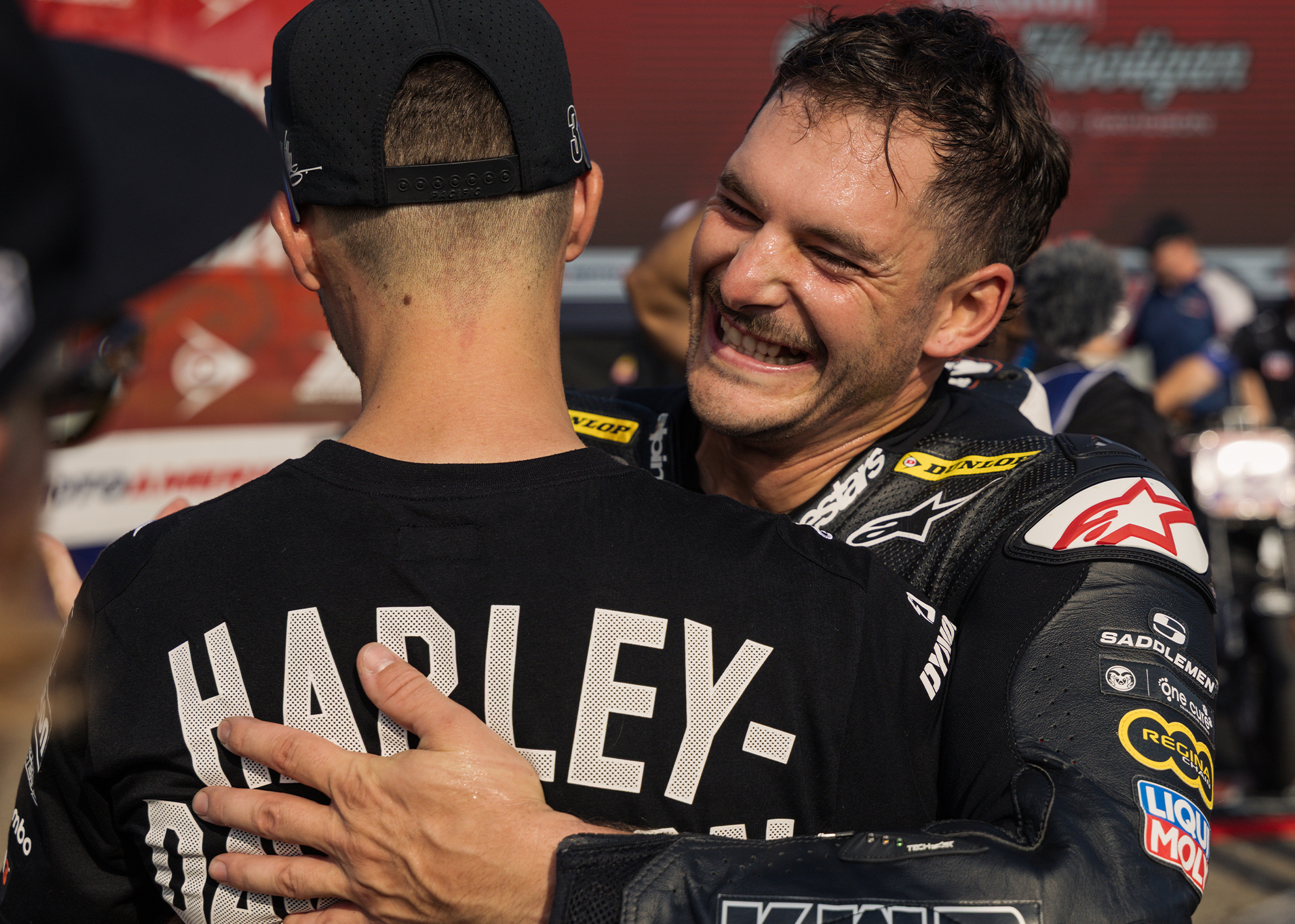 James Rispoli celebrates with a hug, smiling broadly in his Harley-Davidson racing leathers after a race.