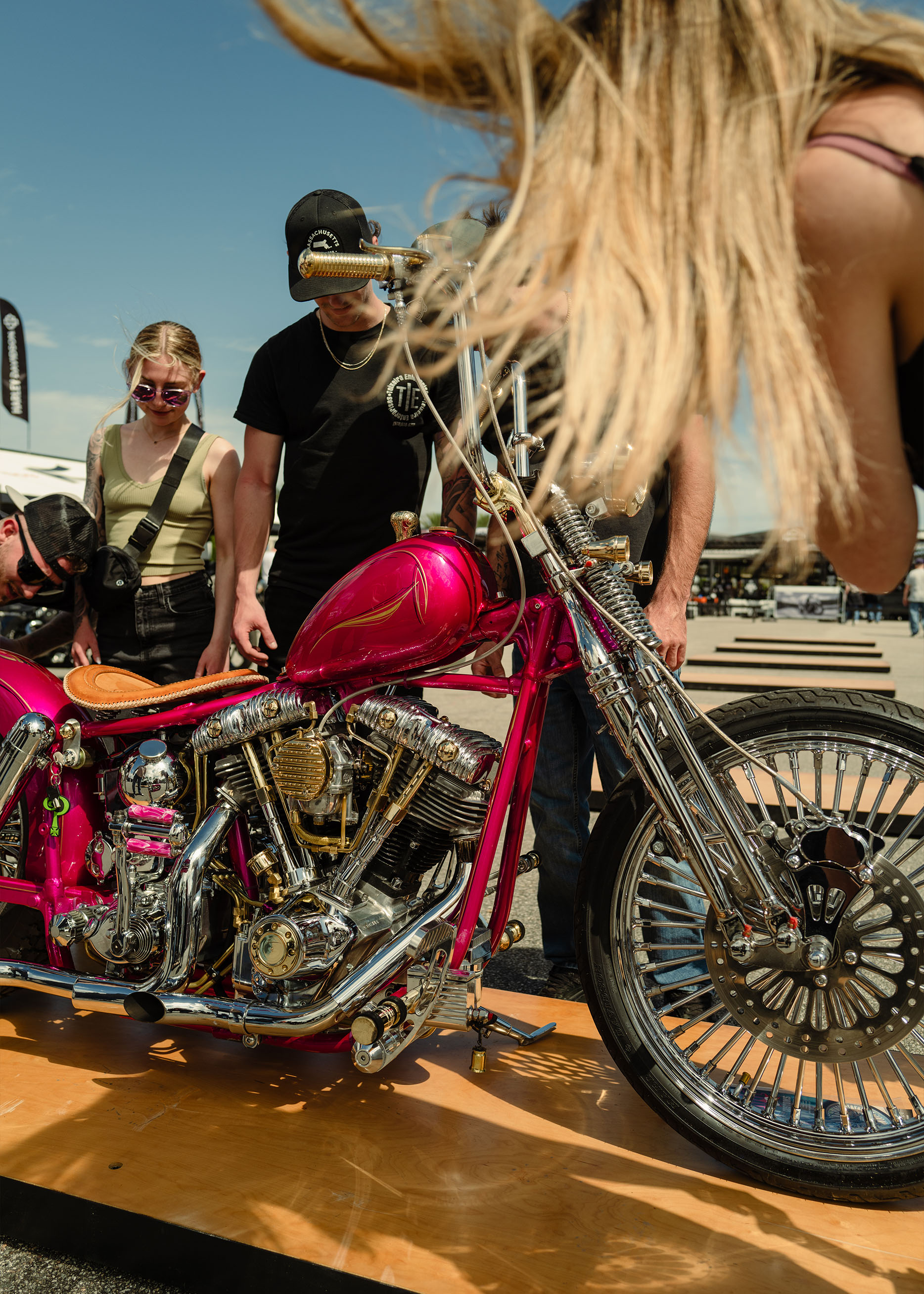 A group of people admire a pink shovelhead chopper