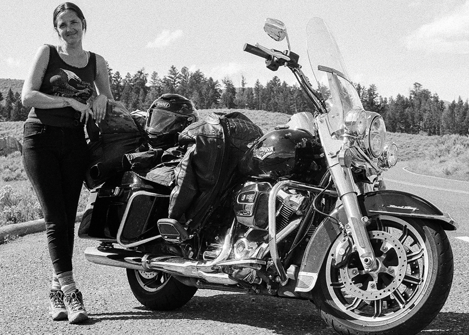 A woman smiles leaning against a motorcycle getting packed up for a ride 