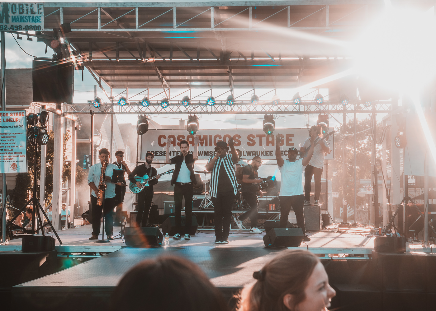 Band performing on outdoor stage with bright lights and crowd in foreground