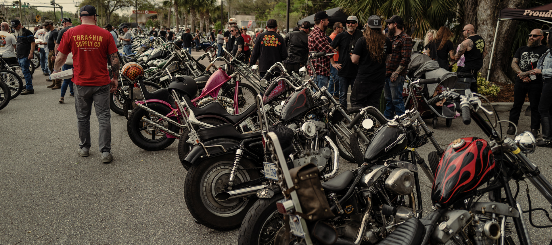 A line of choppers parked outside with people gathered around 