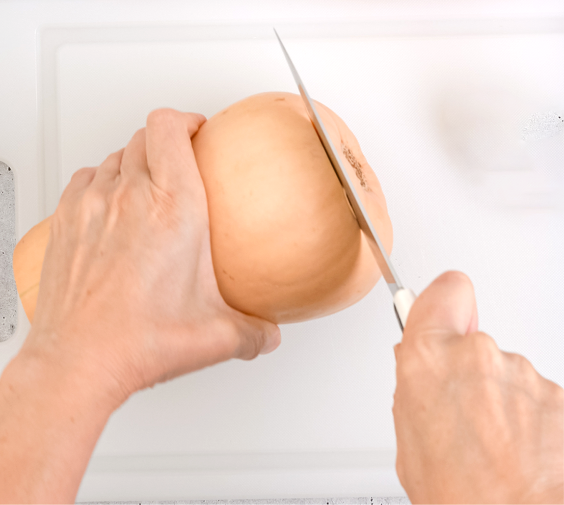 Photo d’une personne qui coupe la base d’une courge musquée à l’aide d’un couteau. 