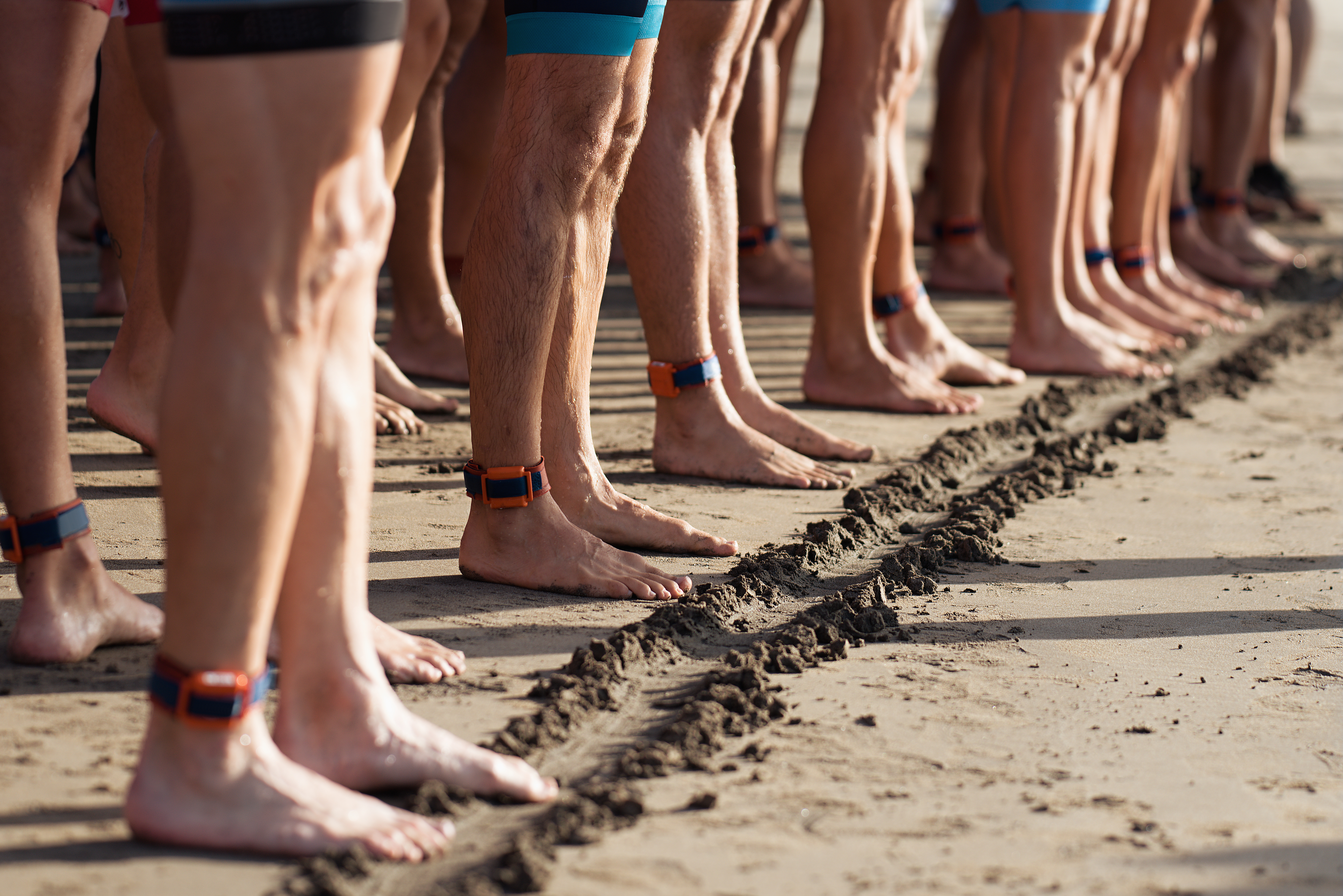 Photo de pieds nus de nombreux athlètes de triathlon sur une plage de sable.