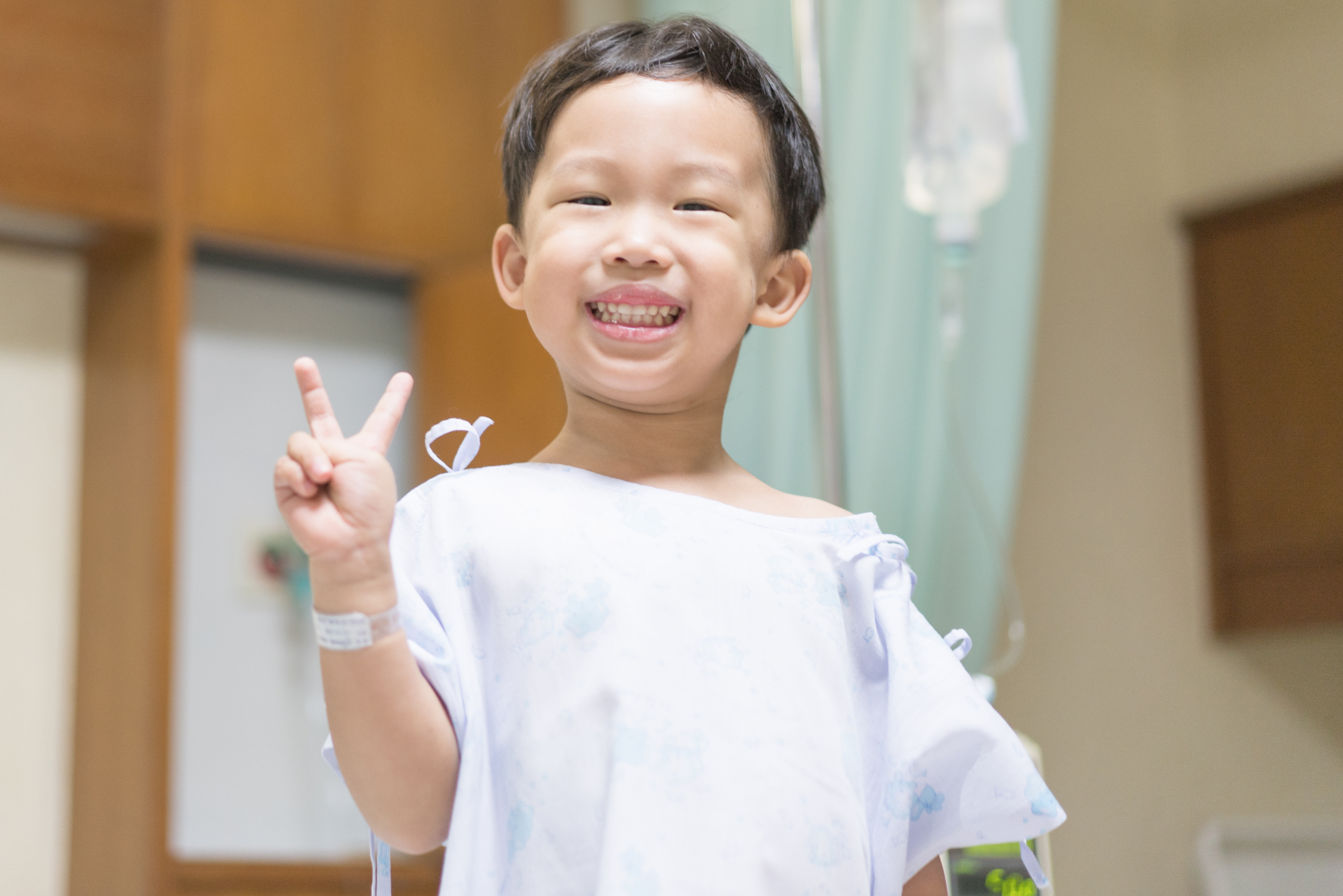 Photo d'un enfant vêtu d'une blouse d'hôpital, faisant le signe de la paix.