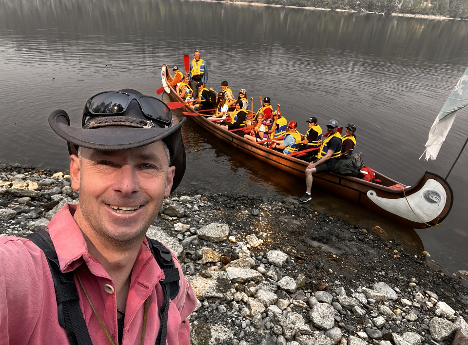 Photo d’André Bernier. Derrière lui, on peut voir un lac et des gens dans un canot.  