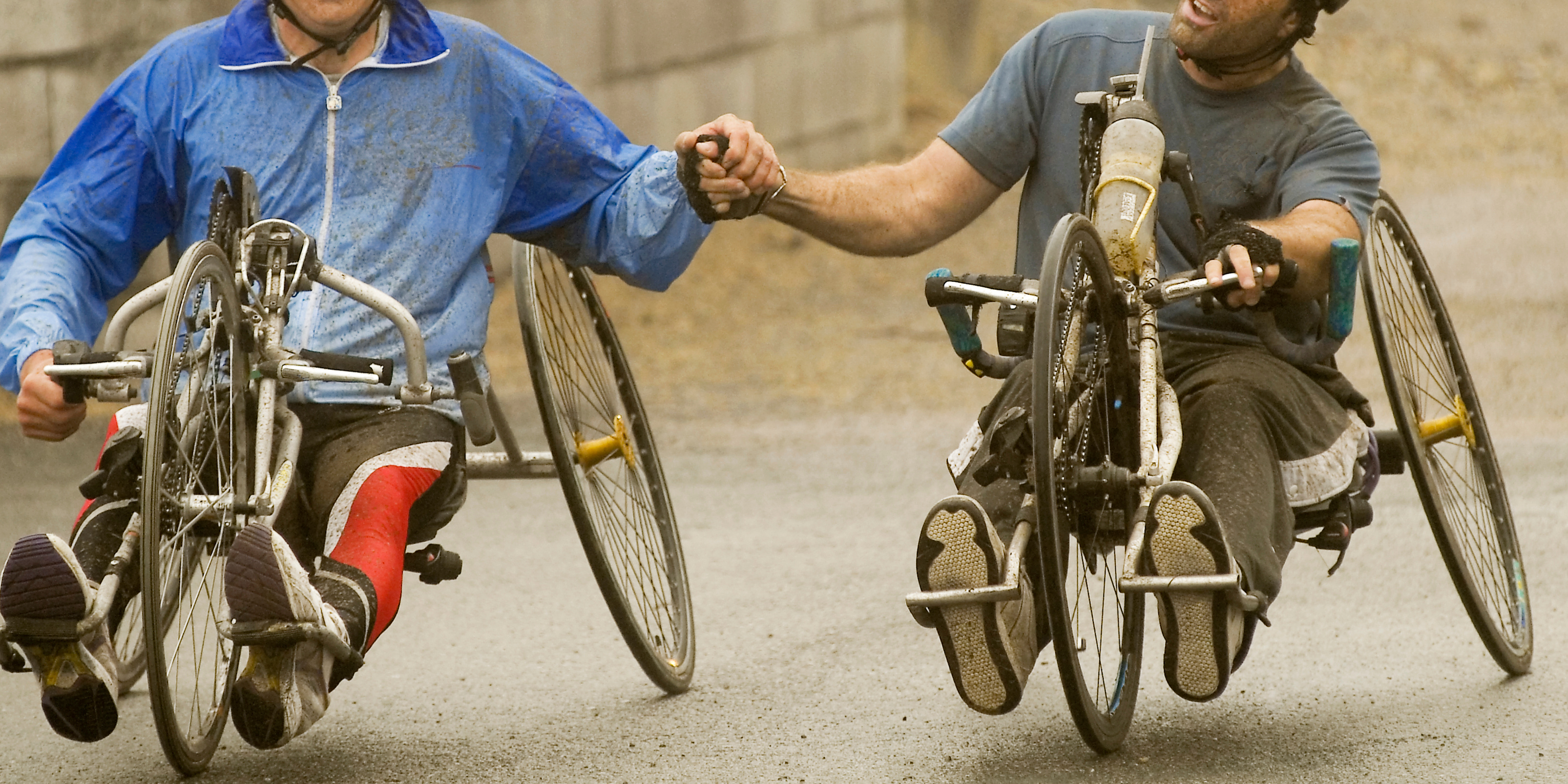 Photo de deux hommes faisant du vélo à quatre roues. Ils se serrent la main. 