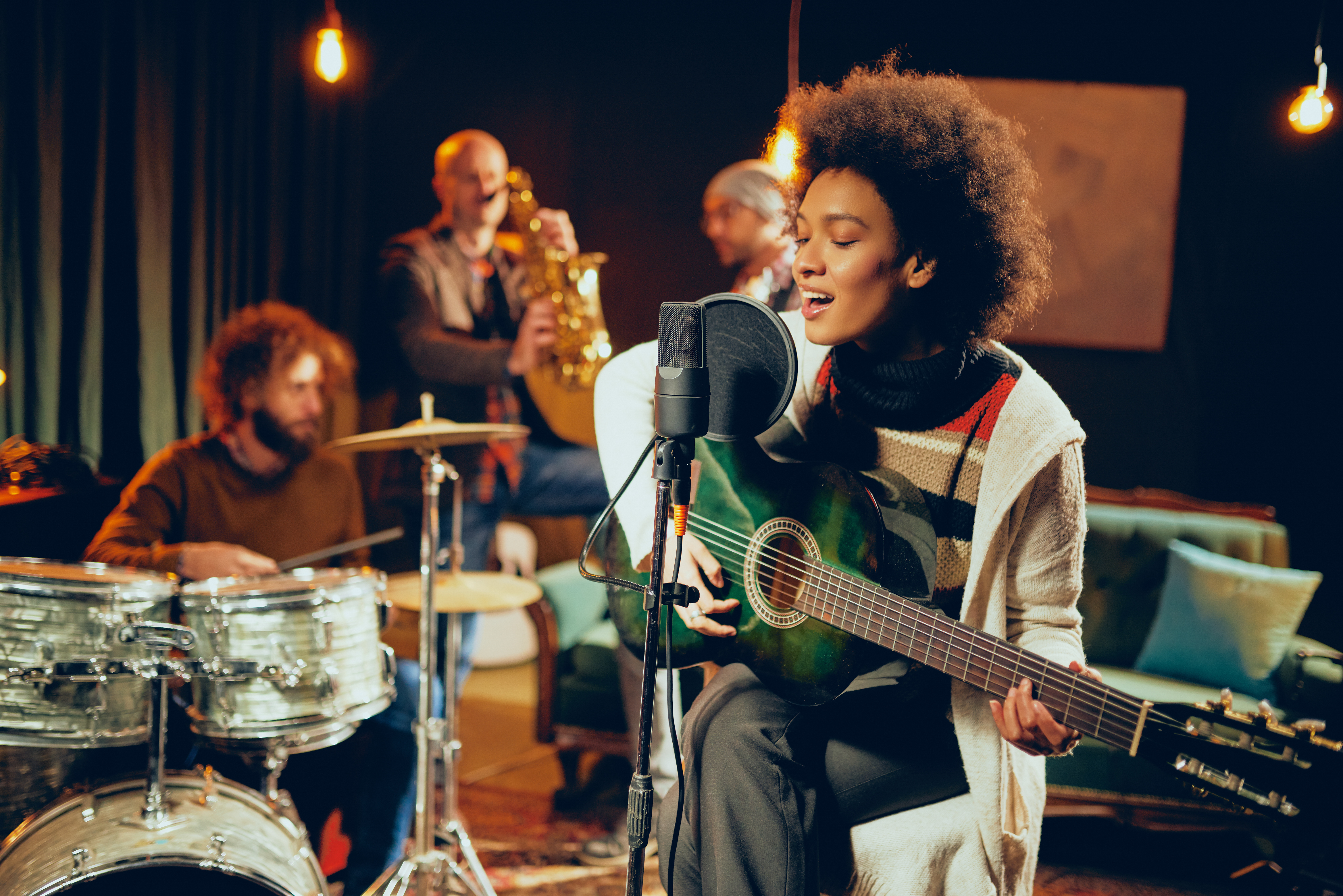 Photo d’une jeune femme qui chante dans un spectacle. Elle joue aussi de la guitare.  