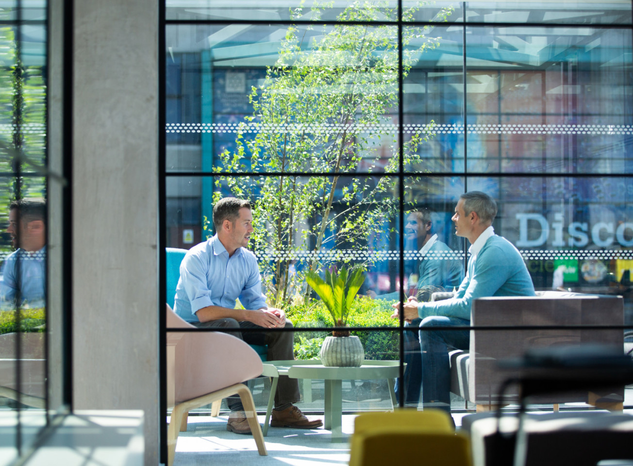 Man and a woman sat at a desk outside smiling while working on a laptop