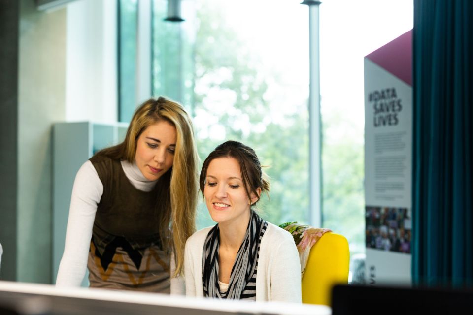 Two women sat at a desk smiling while working on a laptop