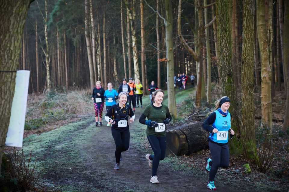 women running a charity race through woodland at alderley park